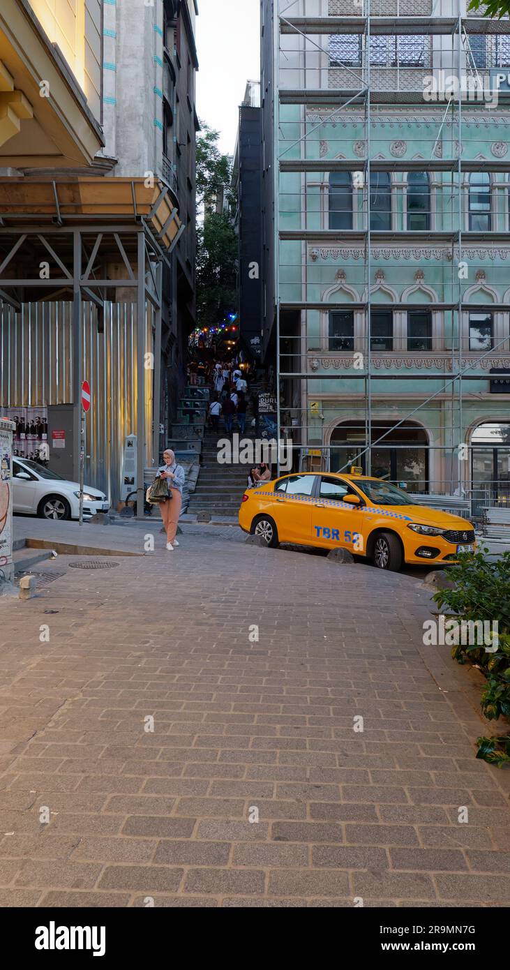 Leute, die abends im Viertel Galata Treppen hinaufgehen, während ein gelbes Taxi wartet und eine Frau ihr Telefon überprüft. Istanbul Türkei Stockfoto