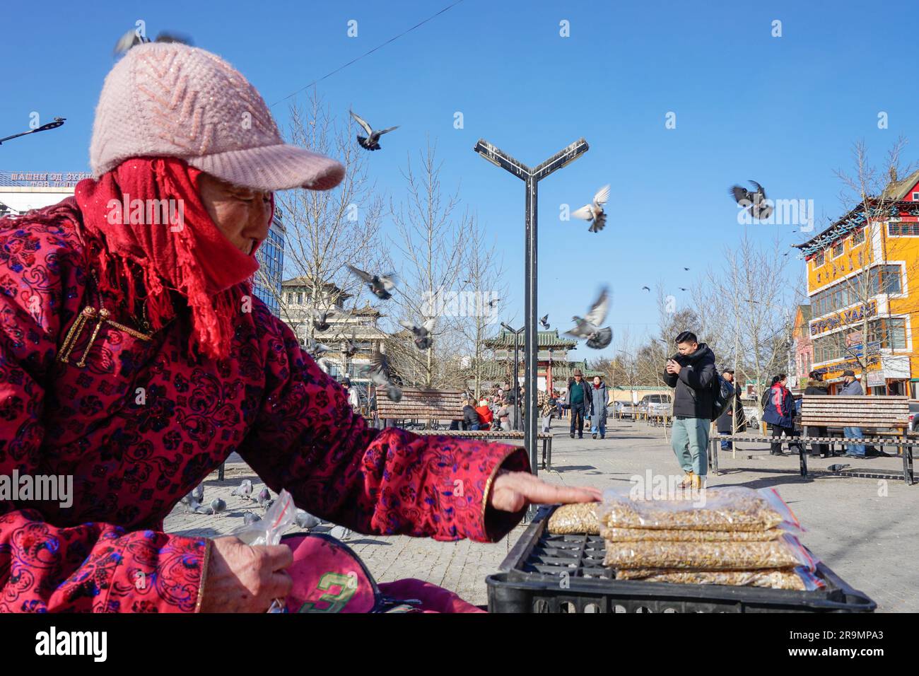Tseveen Ravdan verkauft Reis an Menschen, die Tauben füttern, außerhalb des Klosters Gandantegchenlin, einem zentralen mongolischen buddhistischen Kloster in Ulaanbaatar am 25. Februar 2023. (Nansalmaa Oyunchimeg/Global Press Journal) Stockfoto