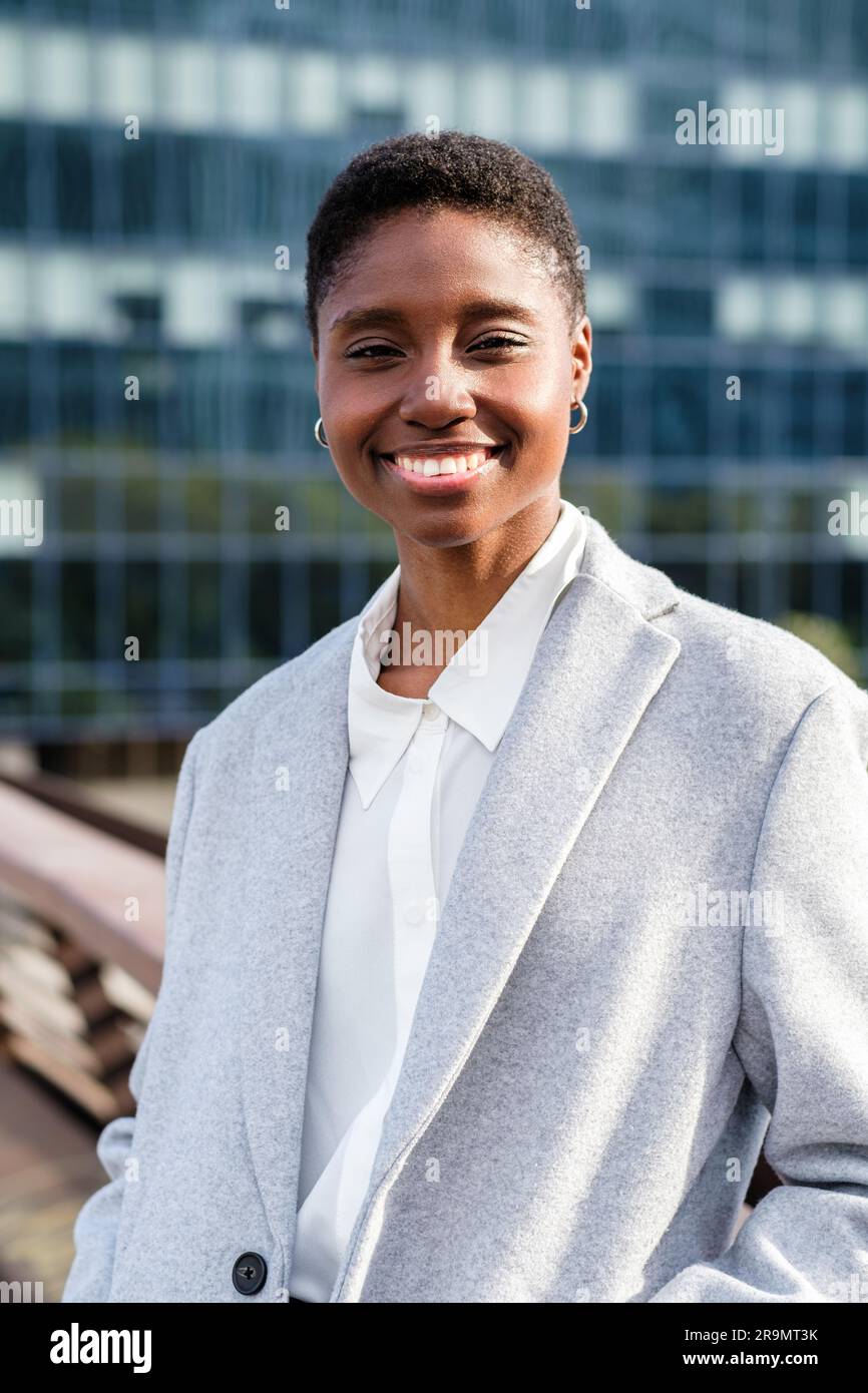 Vertikales Porträt einer jungen afrikanerin, die auf einer Brücke des Finanzdistrikts wohnt. Sie sieht in die Kamera und lächelt Stockfoto