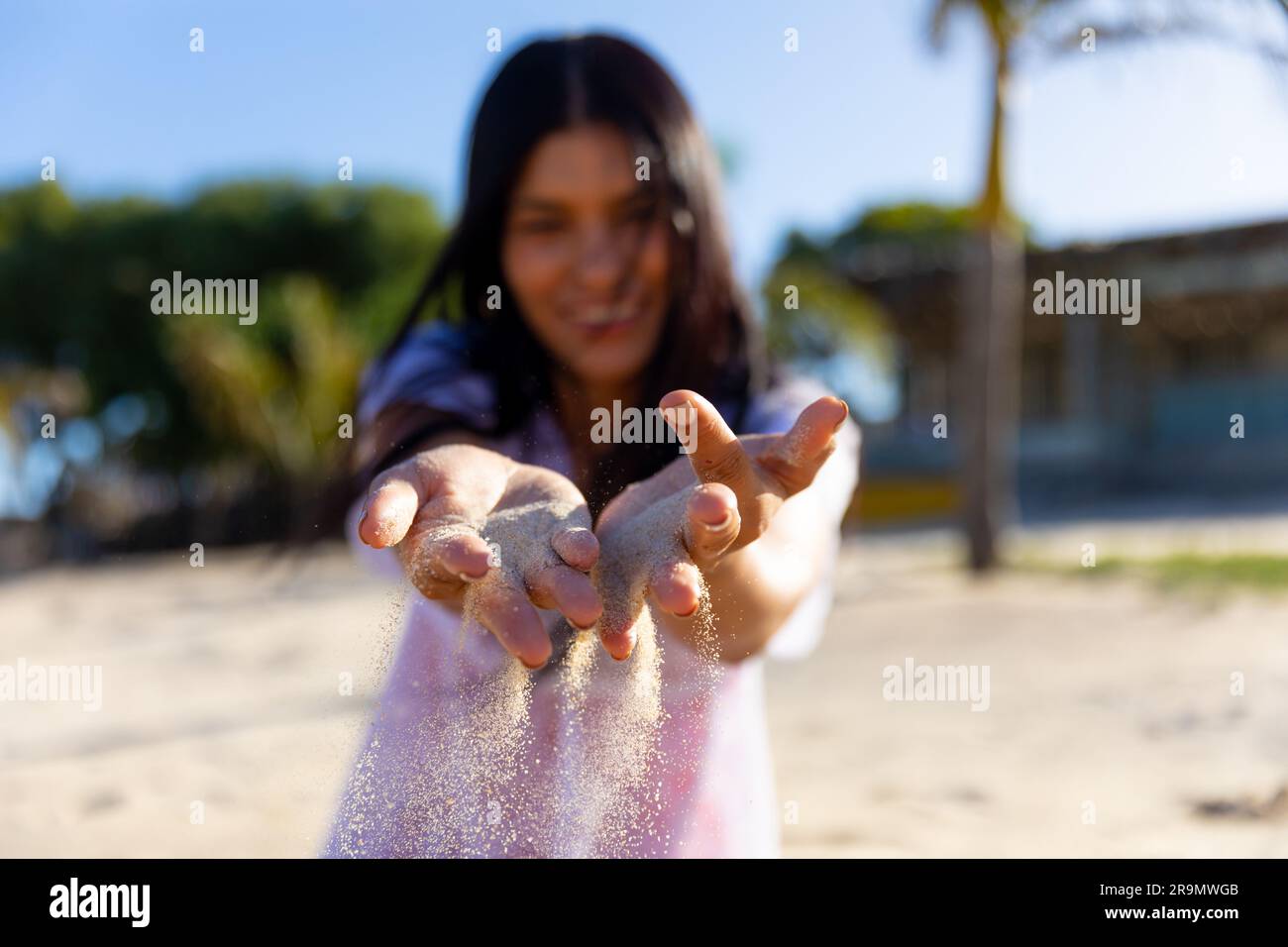 Lächelnde, birassische Frau, die mit Sand am sonnigen Strand spielt, selektive Konzentration Stockfoto