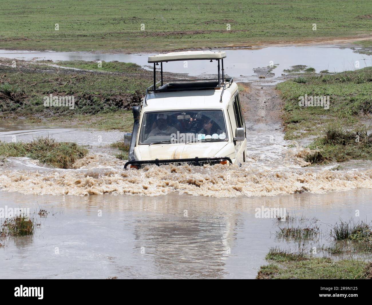 Afrika, Tansania, Serengeti-Nationalpark, Safari-Touristen in einem offenen Land Rover, der eine Wasserbarriere überquert Stockfoto