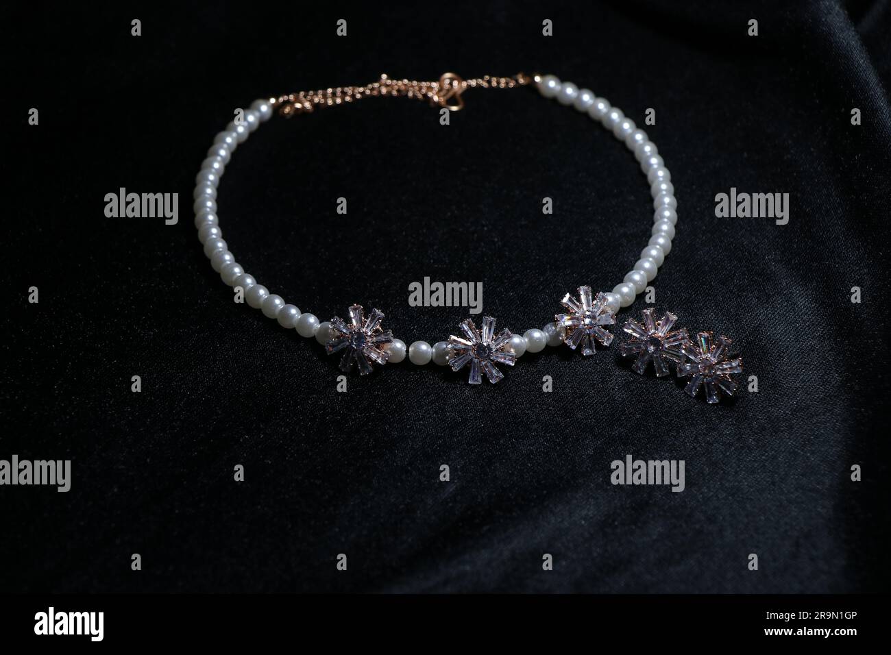 Damenhalskette mit kleinem Ohrring auf fesselndem schwarzem Hintergrund Stockfoto