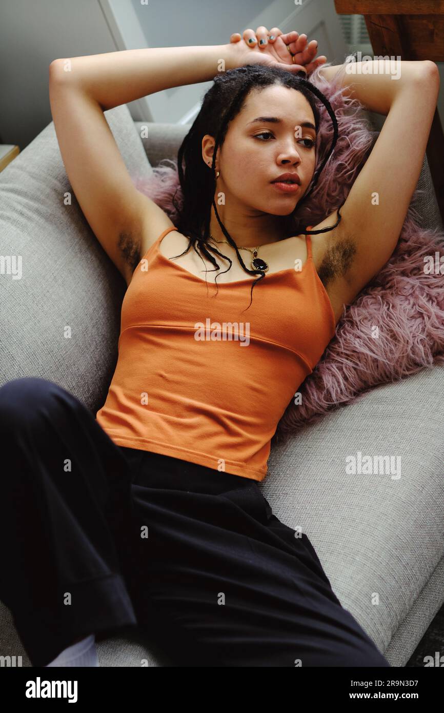 Porträt einer jungen Frau mit erhobenen Armen und Achselhaaren, natürlichem Körper, entspannt auf dem Sofa Stockfoto