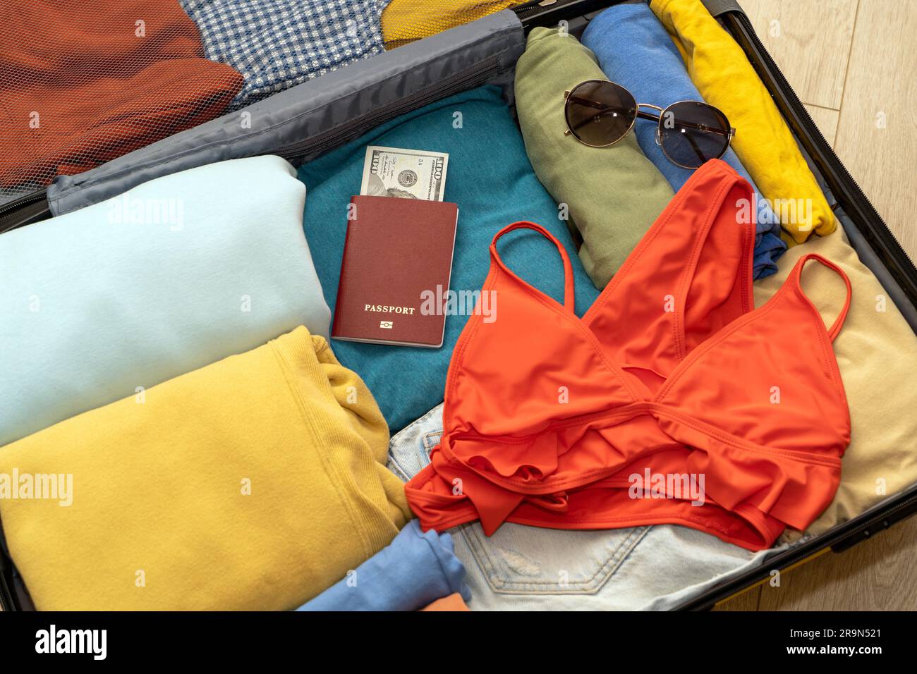 Gefaltete Damenbekleidung, Pässe mit Dollars, Badeanzug und Sonnenbrille in einem Koffer auf Holzhintergrund, von oben nach unten. Verpackung für Fahrt bei Stockfoto