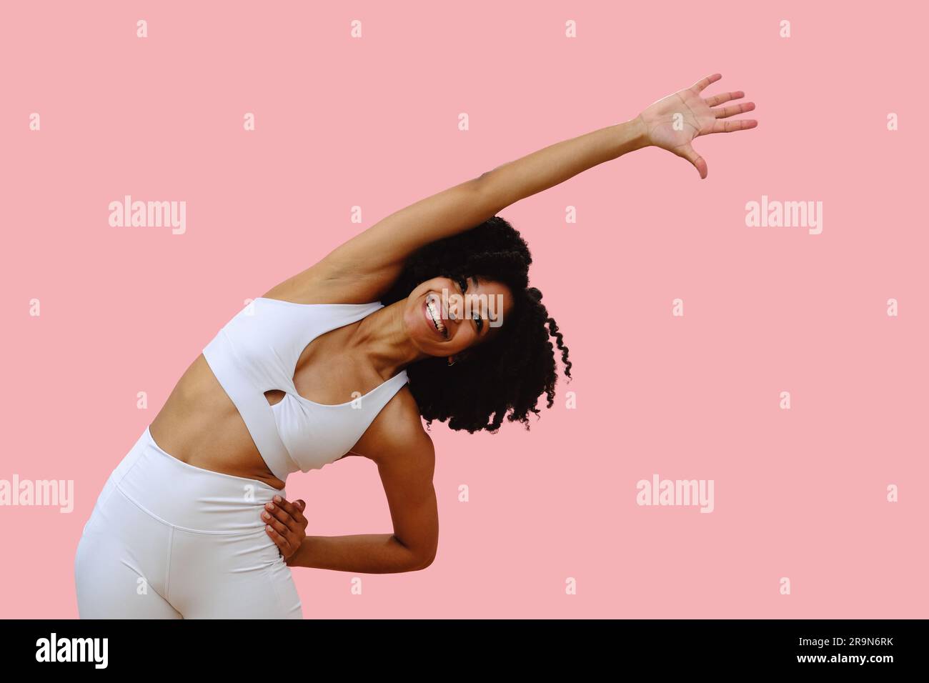 Porträt einer jungen schwarzen Frau, die Sportbekleidung trägt und die Arme ausstreckt, vor pinkfarbenem Studiohintergrund Stockfoto