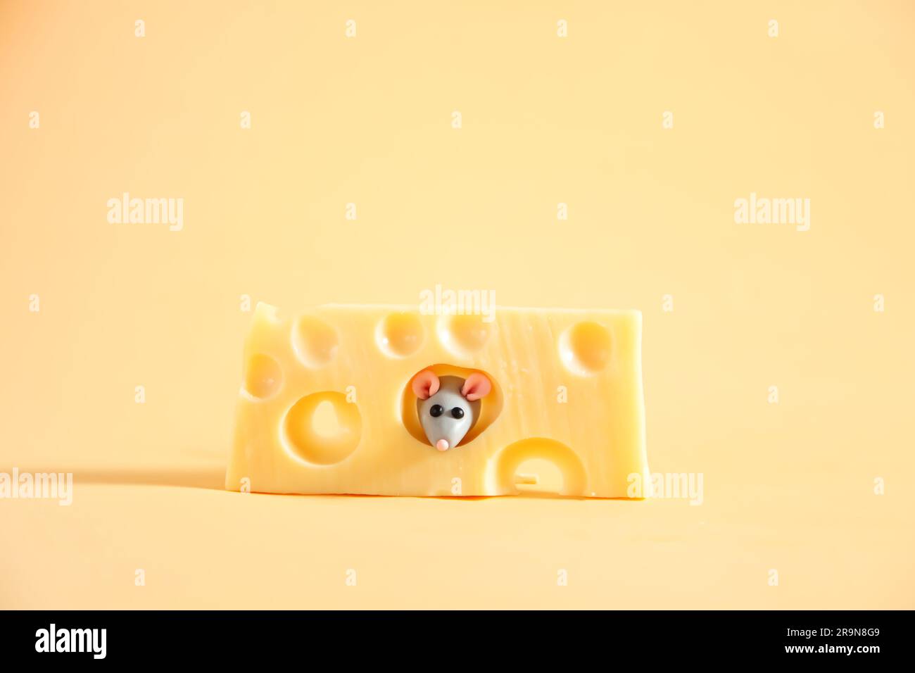 Kleine, graue Plastikmaus und ein Stück Käse mit Löchern. Beiger Hintergrund. Stockfoto