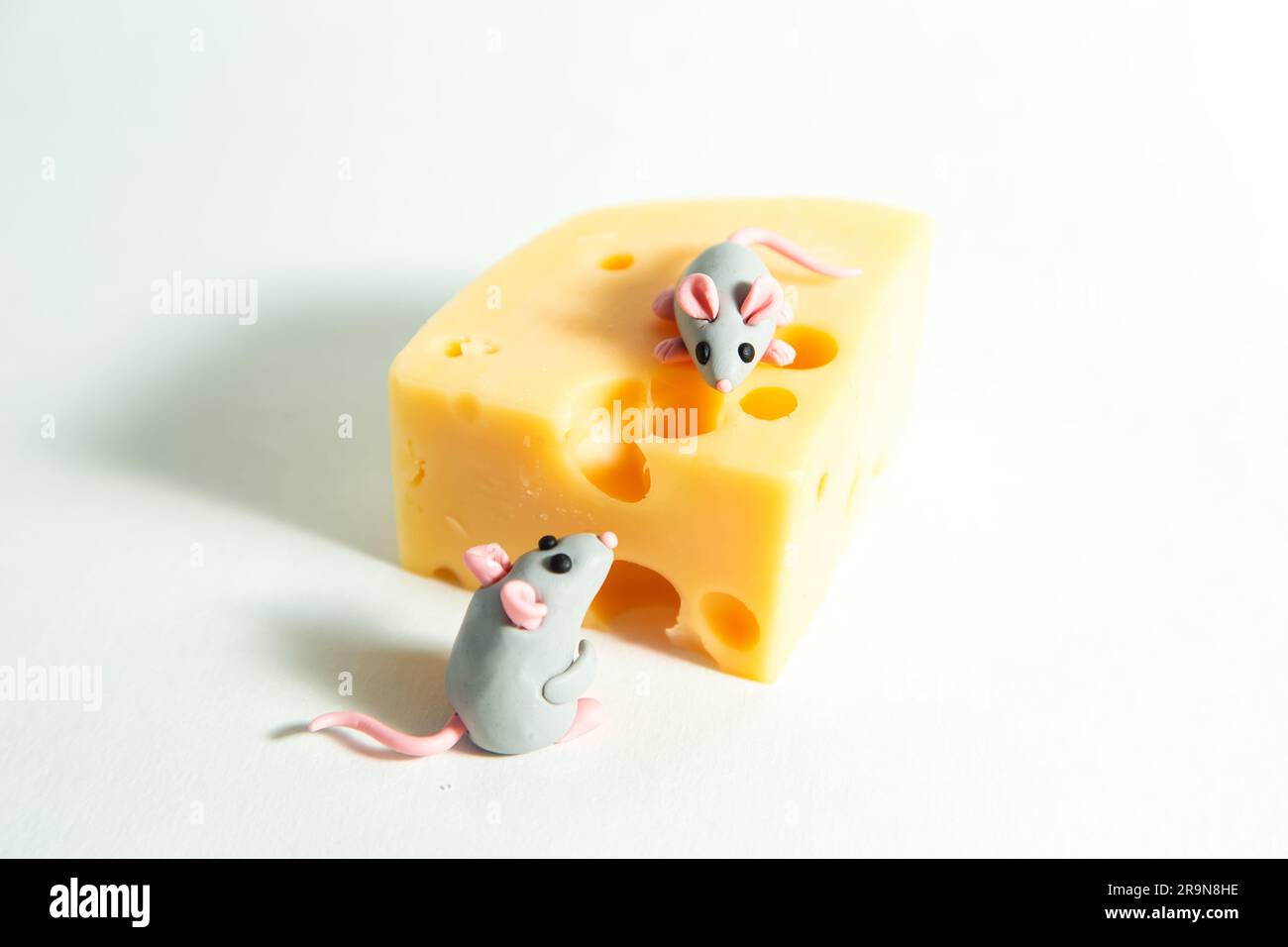 Kleine Plastikmäuse und ein Stück Käse mit Löchern. Weißer Hintergrund. Stockfoto