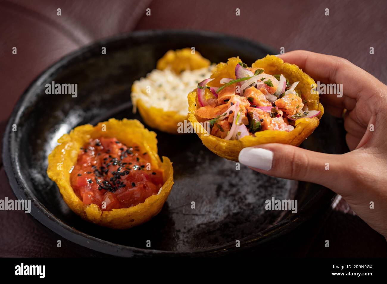 Eine Hand, die frische und gesunde Tacos mit Meeresfrüchten vom schwarzen Teller hält Stockfoto