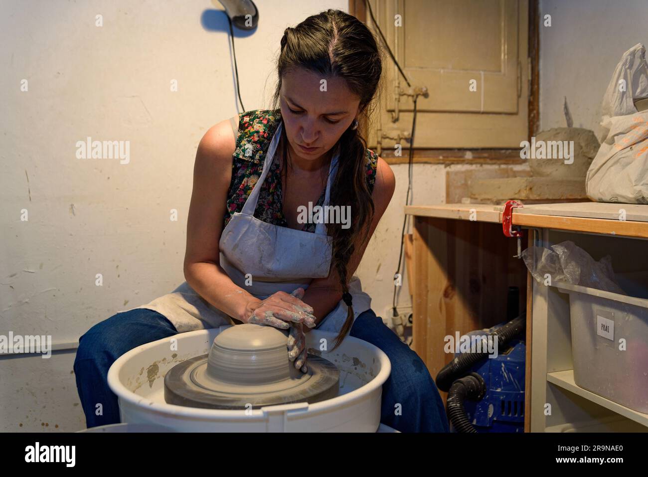 Junge Keramikfrau arbeitet und formt Lehm auf der Drehmaschine oder dem Töpferrad in einer Töpferwerkstatt Stockfoto