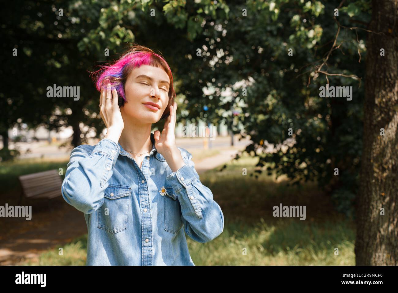 Ein Mädchen mit pinkfarbenen Haaren und Kopfhörern hört im Sommer im Park Musik Stockfoto