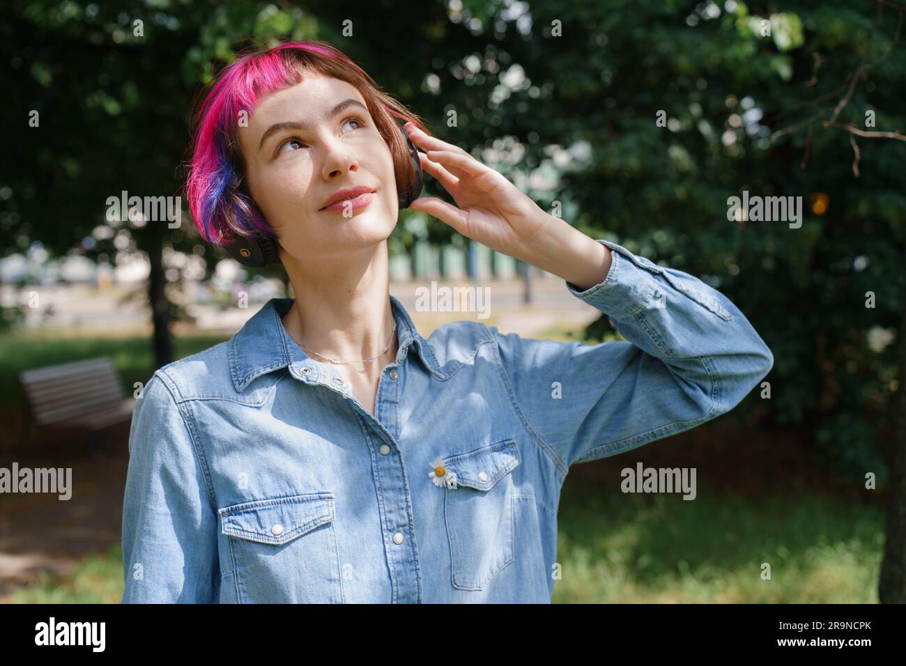 Ein Mädchen mit pinkfarbenen Haaren und Kopfhörern hört im Sommer im Park Musik Stockfoto