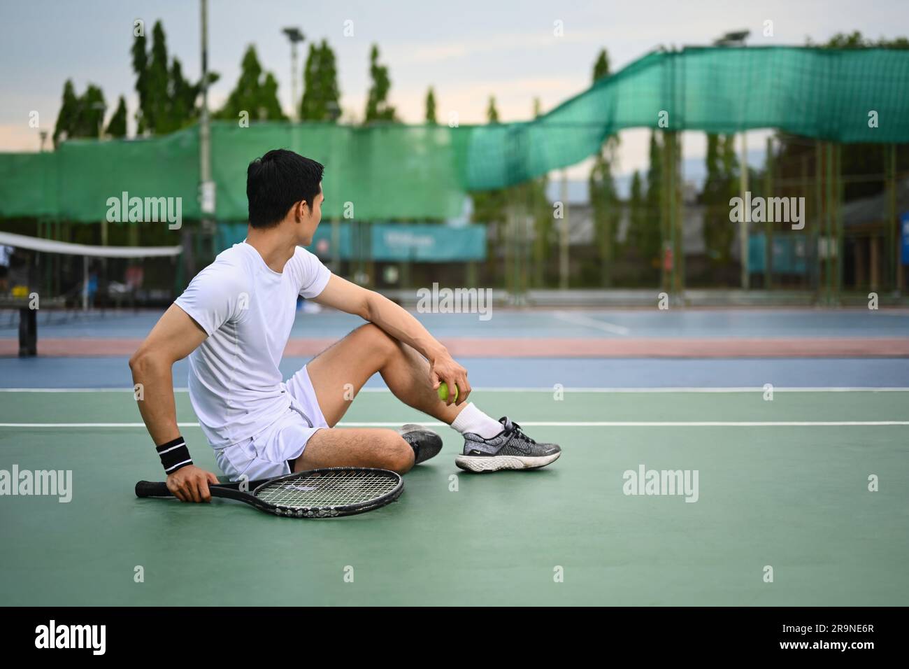 Porträt eines sportlichen Mannes mit einem Tennisschläger, der auf einem Tennisplatz sitzt und wegschaut Stockfoto