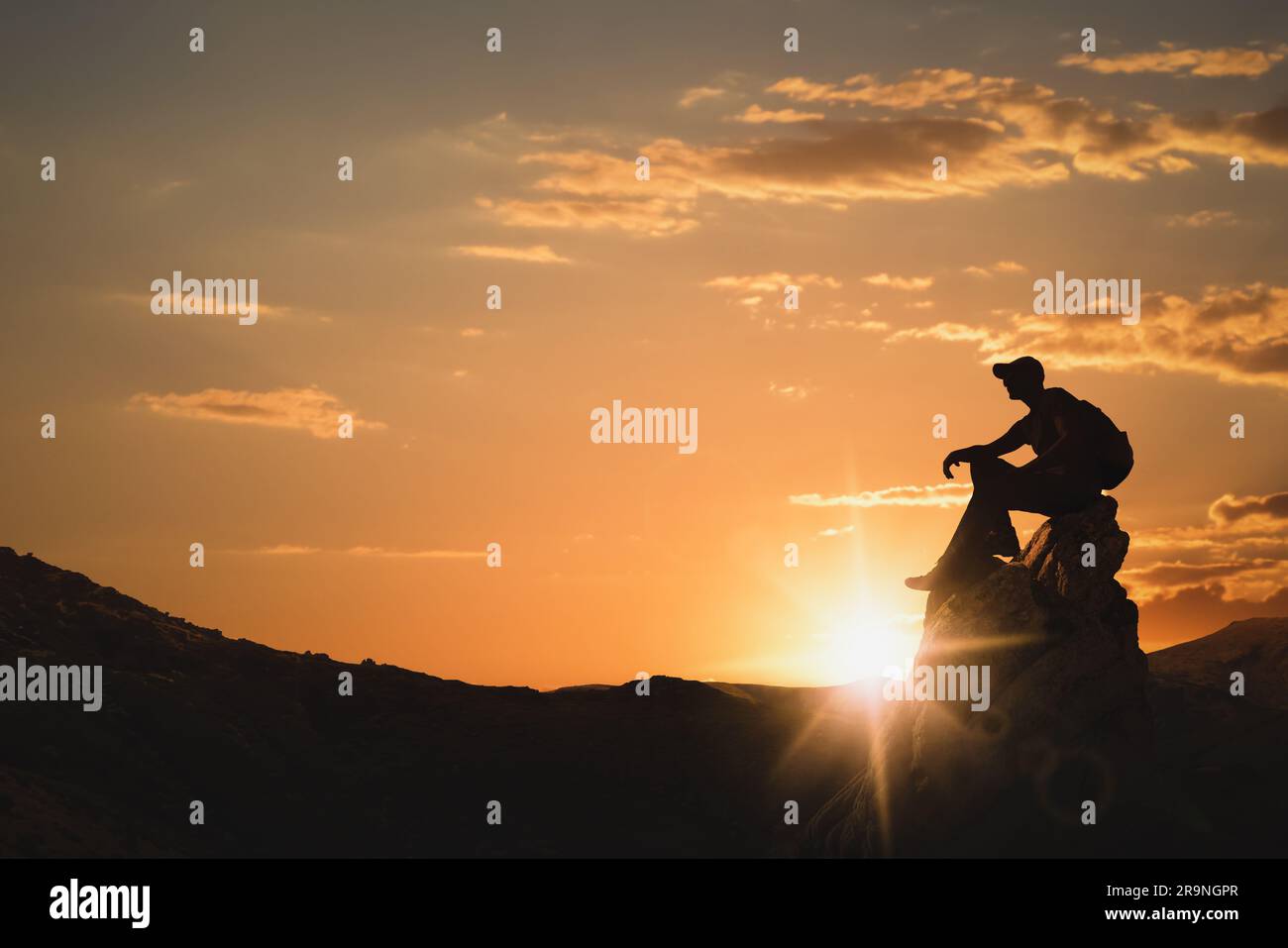 Silhouette eines Mannes mit Rucksack, der bei Sonnenuntergang auf dem Gipfel in den Bergen sitzt. Platz für Text Stockfoto