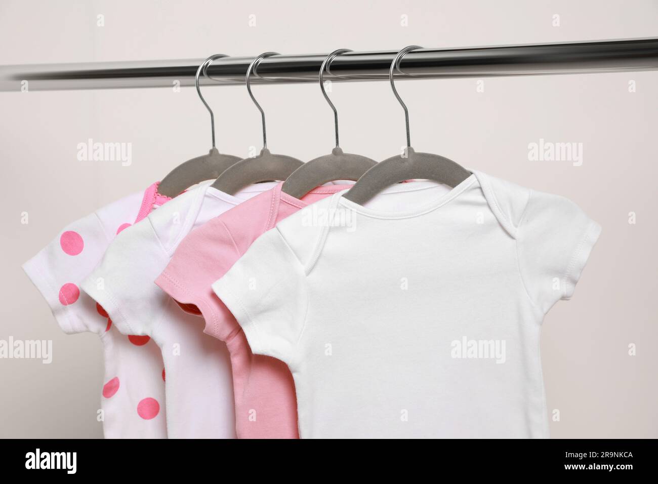 Babykleidung hängt an einem Regal nahe der weißen Wand, Nahaufnahme Stockfoto