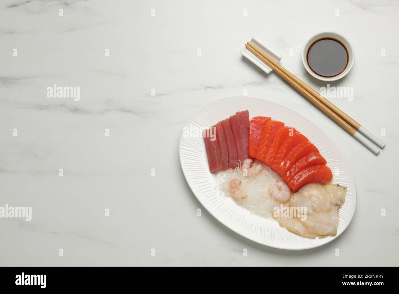 Leckere Lachsscheiben, Garnelen, Funchosa und Thunfisch auf weißem Marmortisch, flach liegend mit Platz für Text. Köstliches Sashimi-Gericht Stockfoto