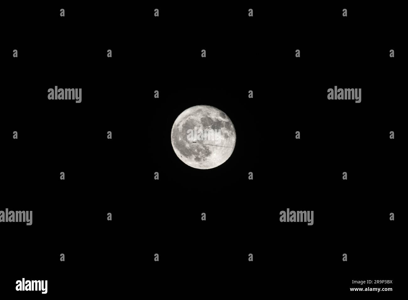Telefotografie des Mondes mit einem Flugzeug, das ihn kreuzt Stockfoto