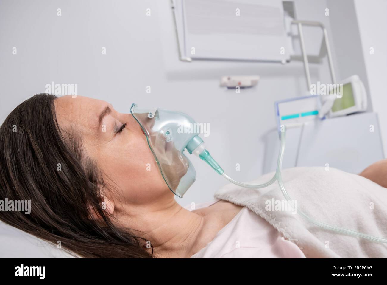 Eine Erwachsene Frau liegt in einer Sauerstoffmaske auf einem Krankenhausbett und wird behandelt. Stockfoto