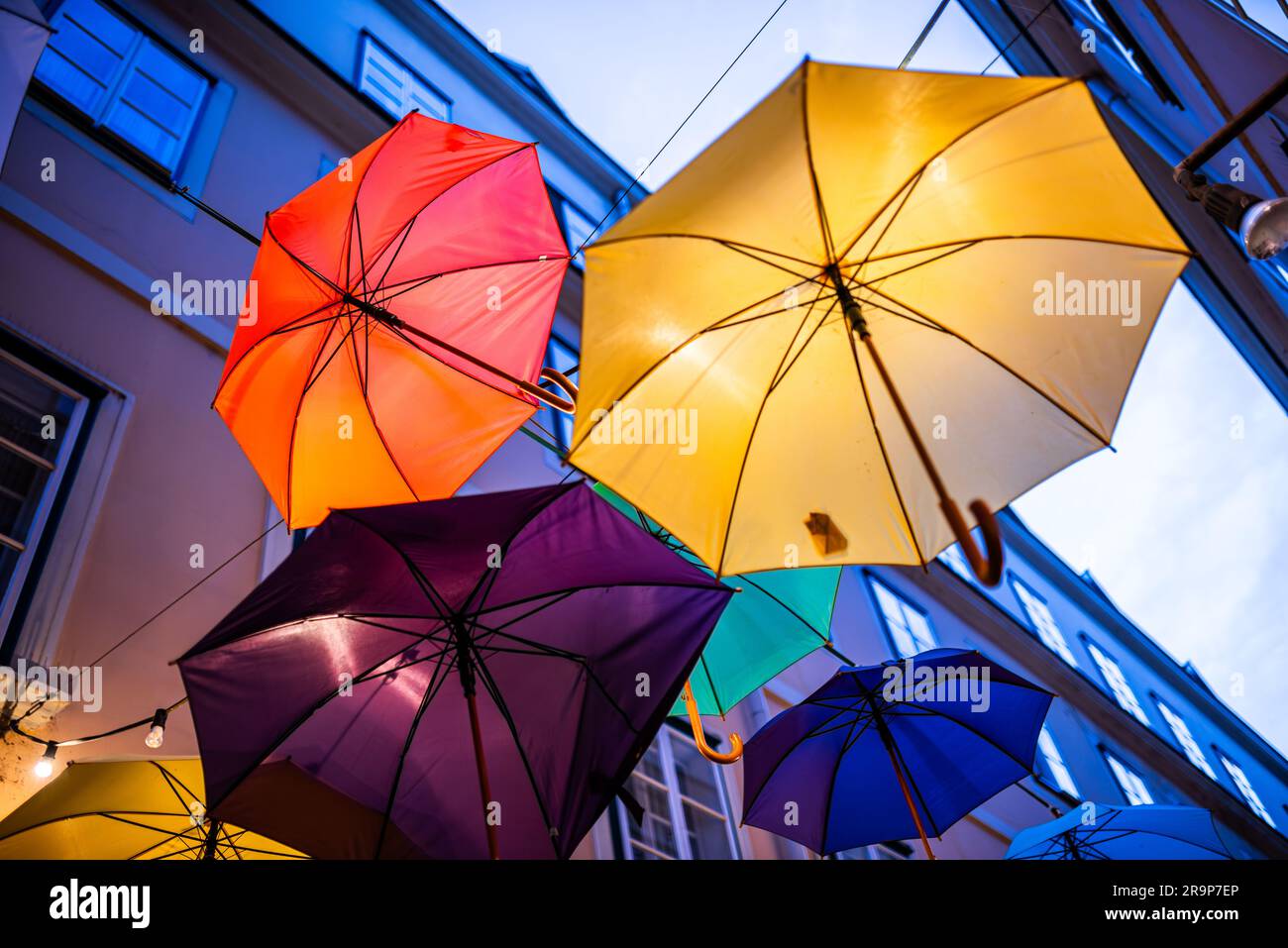 Farbenfrohe Sonnenschirme schmücken eine enge Straße zwischen alten gelben europäischen Gebäuden. Bunte Sonnenschirme sorgen für eine festliche, lustige Kulisse in Wien Stockfoto