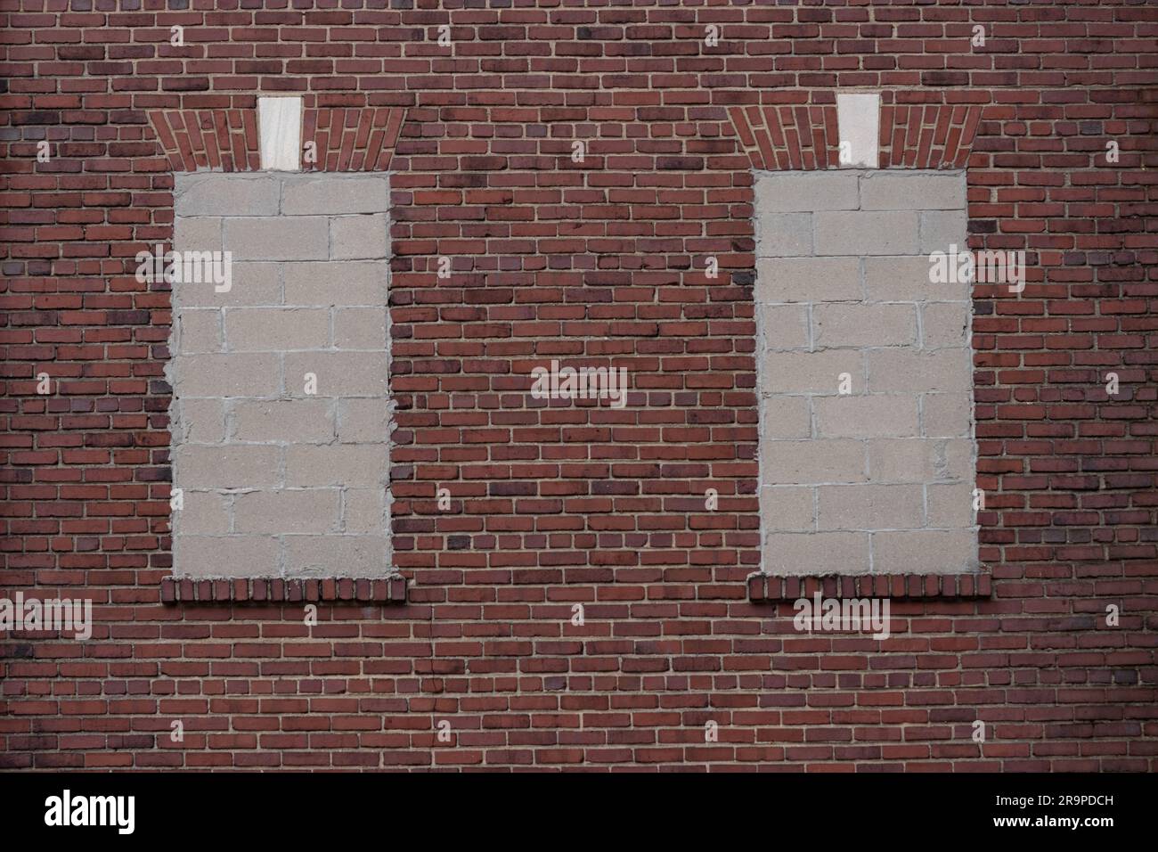 Zwei Fenster, die mit Betonblöcken an einer roten Backsteinwand versiegelt sind, ein dekorativer Fensterkopflintel aus Ziegelstein in Form eines flachen Bogens mit Marmorsteinpflaster Stockfoto