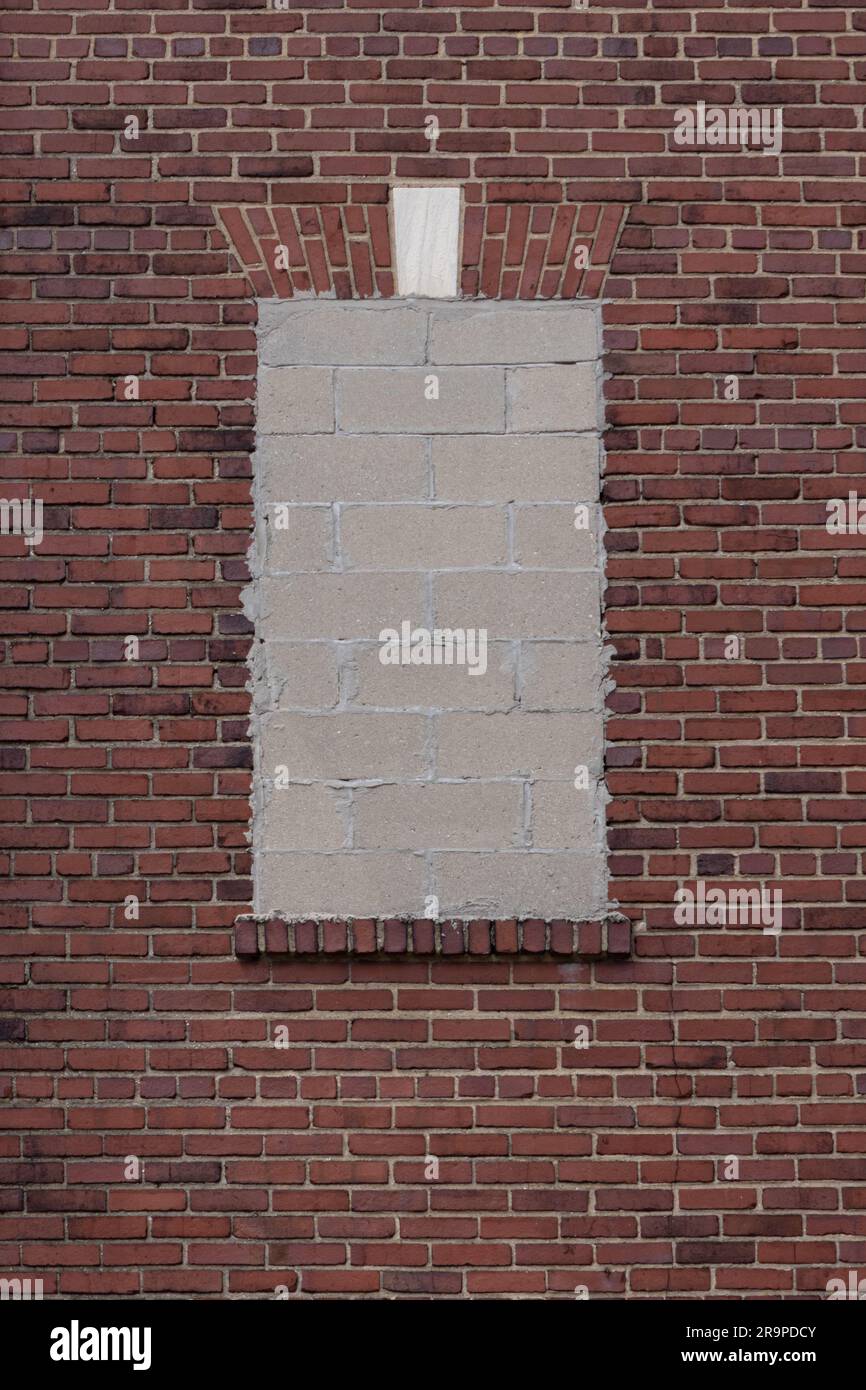 Fenster, das mit Betonblöcken an einer roten Backsteinwand versiegelt ist, mit einem dekorativen Backstein-Fensterkopflintel in Form eines flachen Bogens mit Marmorsteinpflaster Stockfoto