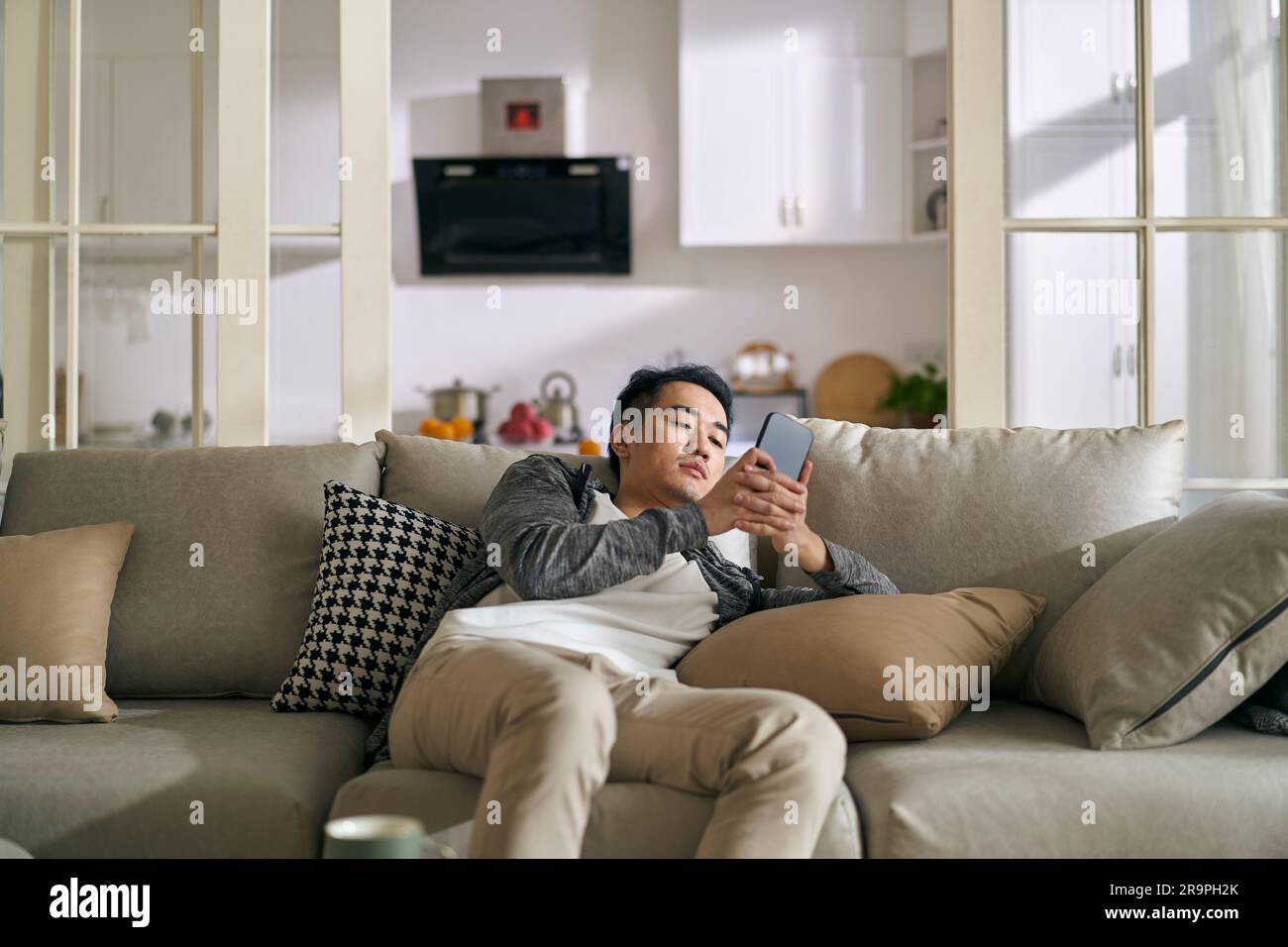 Junger asiatischer Erwachsener, der auf der Couch liegt und zu Hause auf das Handy schaut, Konzept für Smartphone- oder Social-Media-sucht Stockfoto