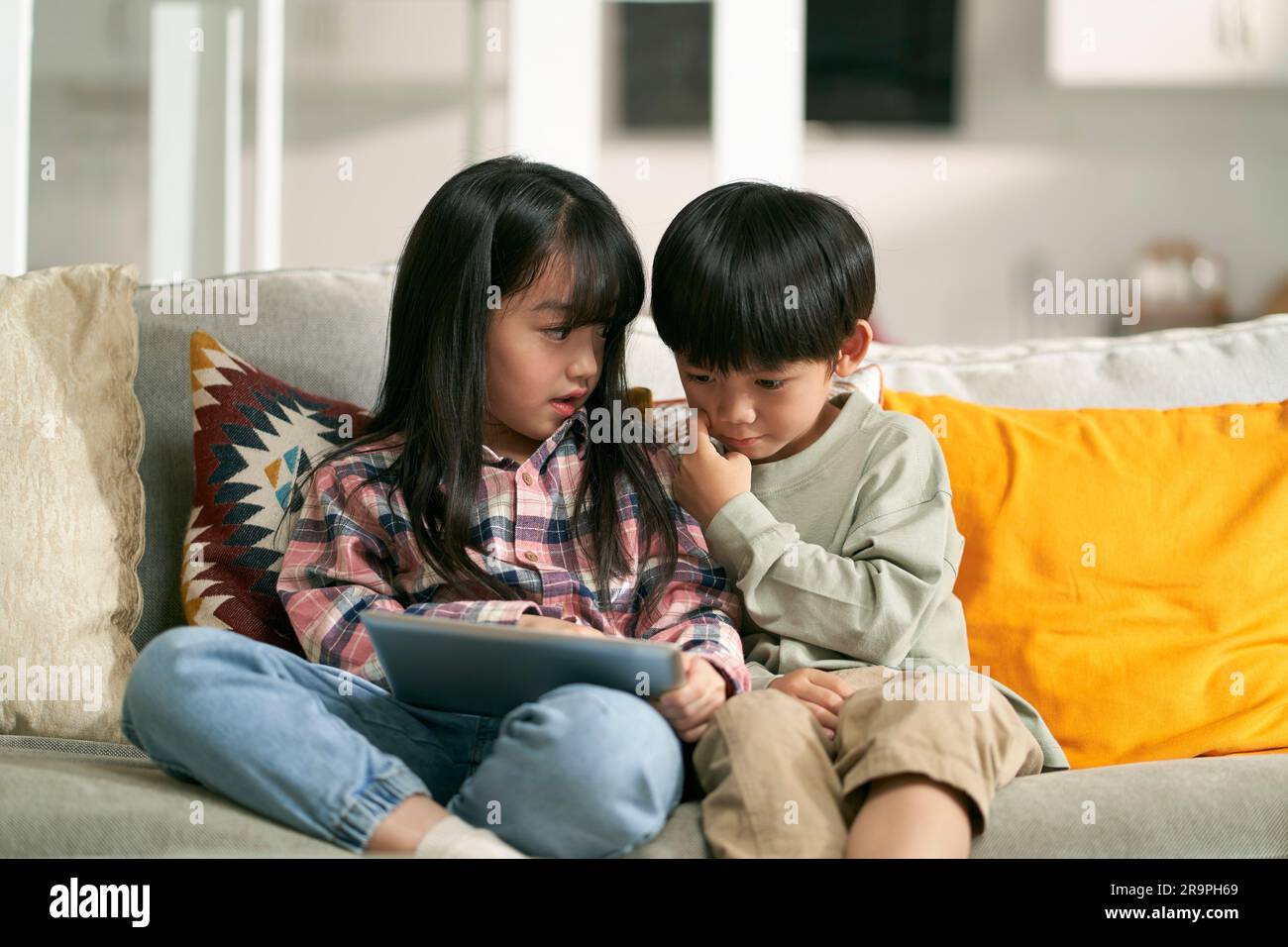 Kleine asiatische Kinder, Bruder und Schwester, die zu Hause auf dem Familientisch sitzen und einen digitalen Tablet-Computer benutzen Stockfoto
