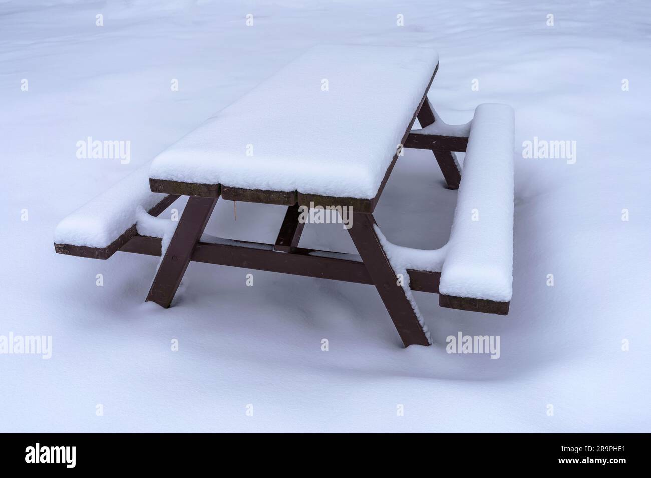 Schneebedeckter Picknicktisch aus Holz im Winter. Stockfoto