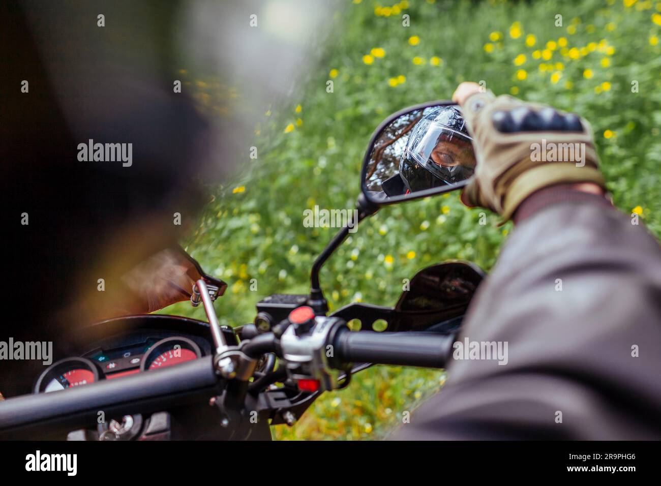 Motorradfahrer, die im Außenspiegel von Motorrädern schauen. Mann in Lederjacke und Helmritt im Sommerwald. Stockfoto