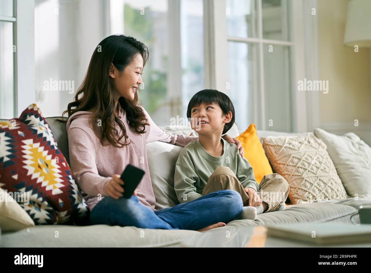 Junge asiatische Mutter, die zu Hause auf dem Familientisch sitzt und ein angenehmes Gespräch mit dem fünfjährigen Sohn führt Stockfoto