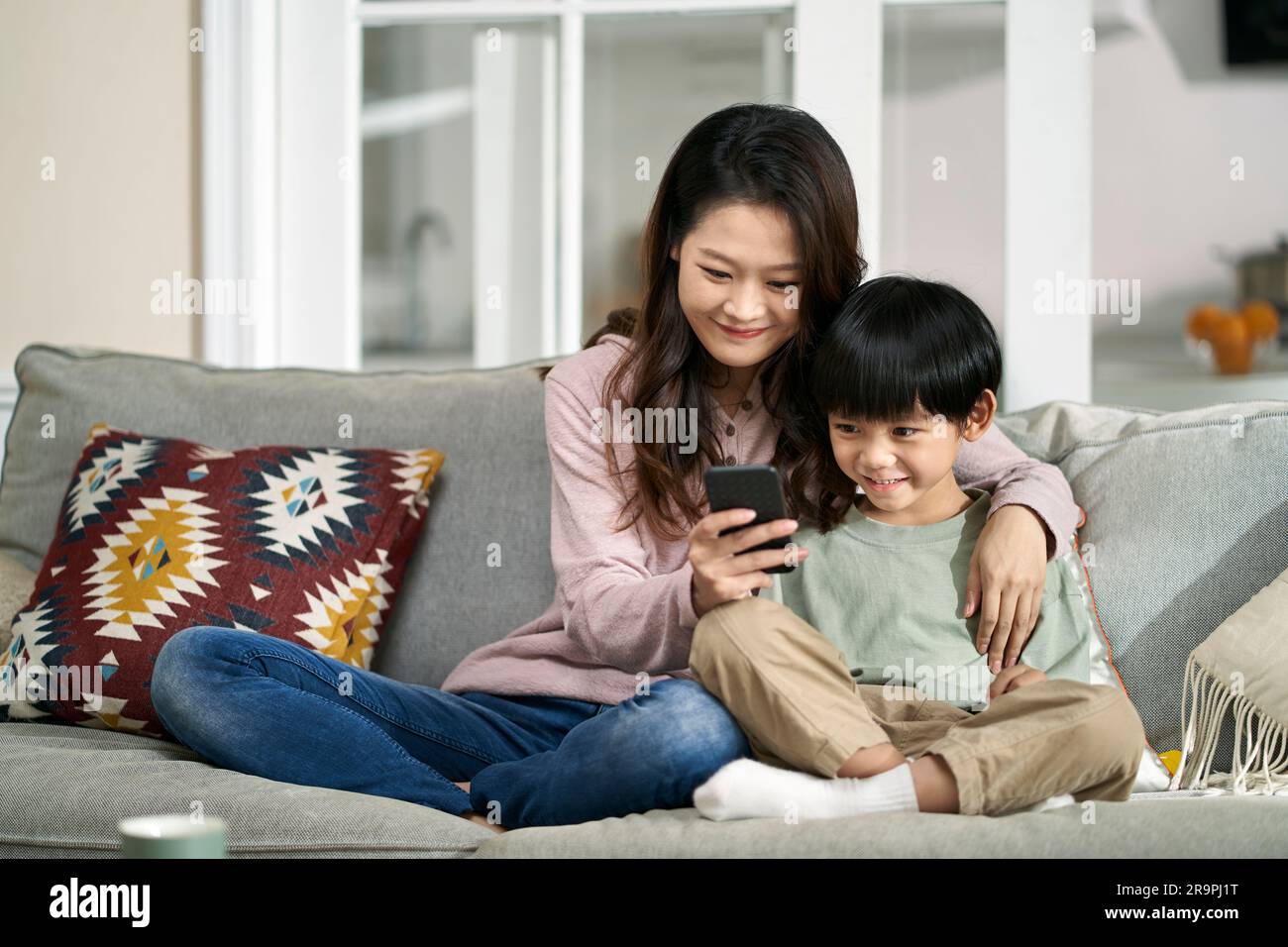 Glückliche asiatische Mutter und Sohn, die auf der Familientisch sitzen und sich Handyfotos anschauen Stockfoto