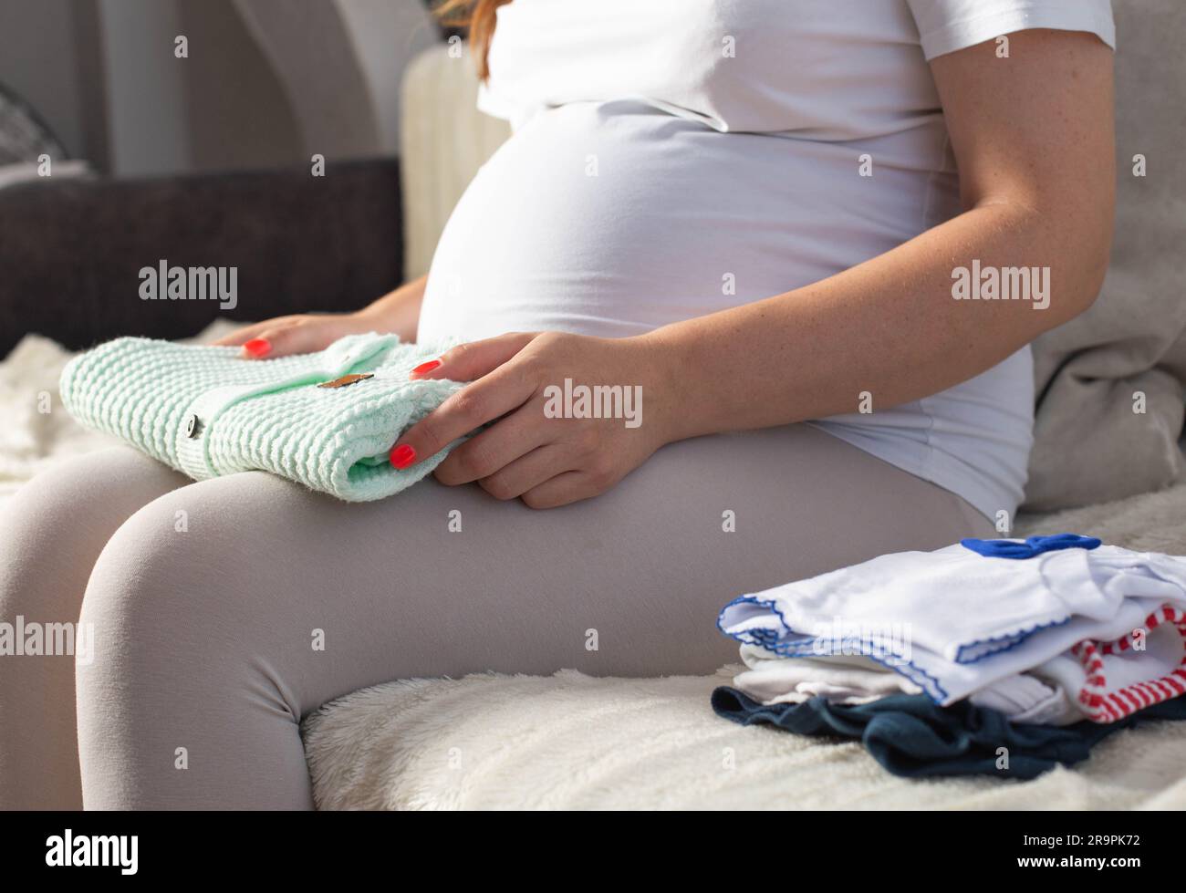 Ein schwangeres Mädchen arrangiert warme Kleidung für ein Neugeborenes. Qualitätskleidung für Babys im Krankenhaus. Stockfoto