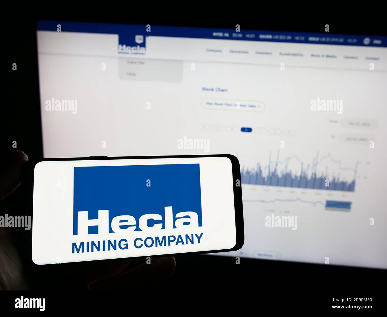 Person, die ein Mobiltelefon mit dem Logo des amerikanischen Unternehmens Hecla Mining Company auf dem Bildschirm vor der Webseite hält. Konzentrieren Sie sich auf das Display des Telefons. Stockfoto