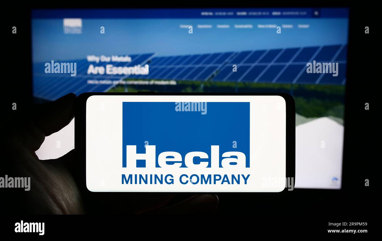 Person, die ein Mobiltelefon mit dem Logo des US-amerikanischen Unternehmens Hecla Mining Company auf dem Bildschirm vor der Webseite hält. Konzentrieren Sie sich auf das Display des Telefons. Stockfoto