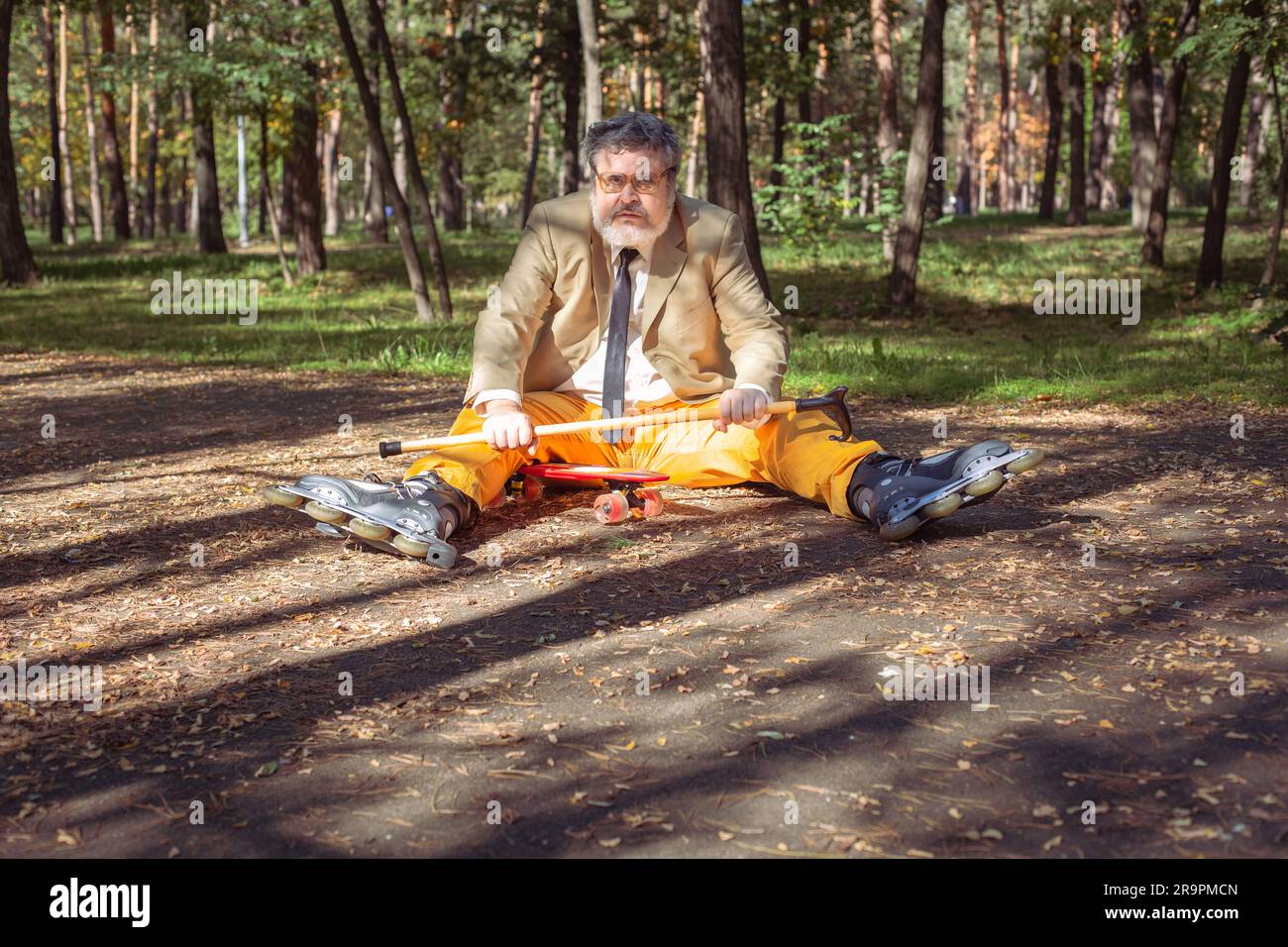 Der lustige alte Mann fährt Rollschuh im Park. Ein aktiver Großvater mit Spazierstock tanzt und macht Gesichter. Großvater mit weißem Bart. Stockfoto