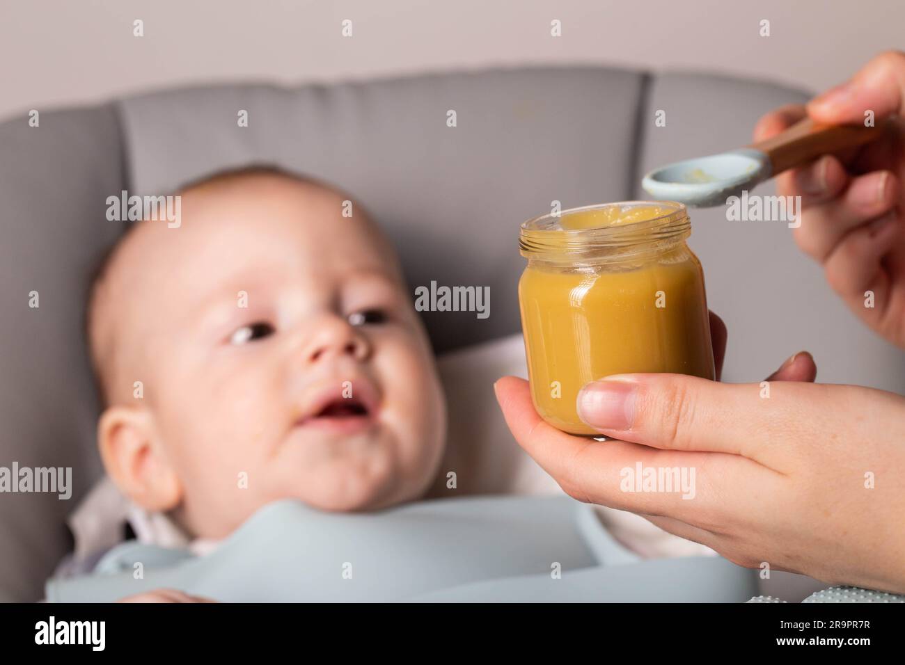 Die Mutter hält ein Glas Gemüsepüree vor dem Hintergrund eines 6 Monate alten Babys. Erste Nahrung für Babys. Stockfoto