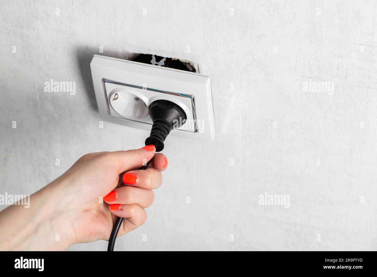 Das Mädchen zieht fälschlicherweise den Stecker aus der Steckdose und unterbricht die Steckdose. Stromschlaggefahr. Platz für Text kopieren Stockfoto