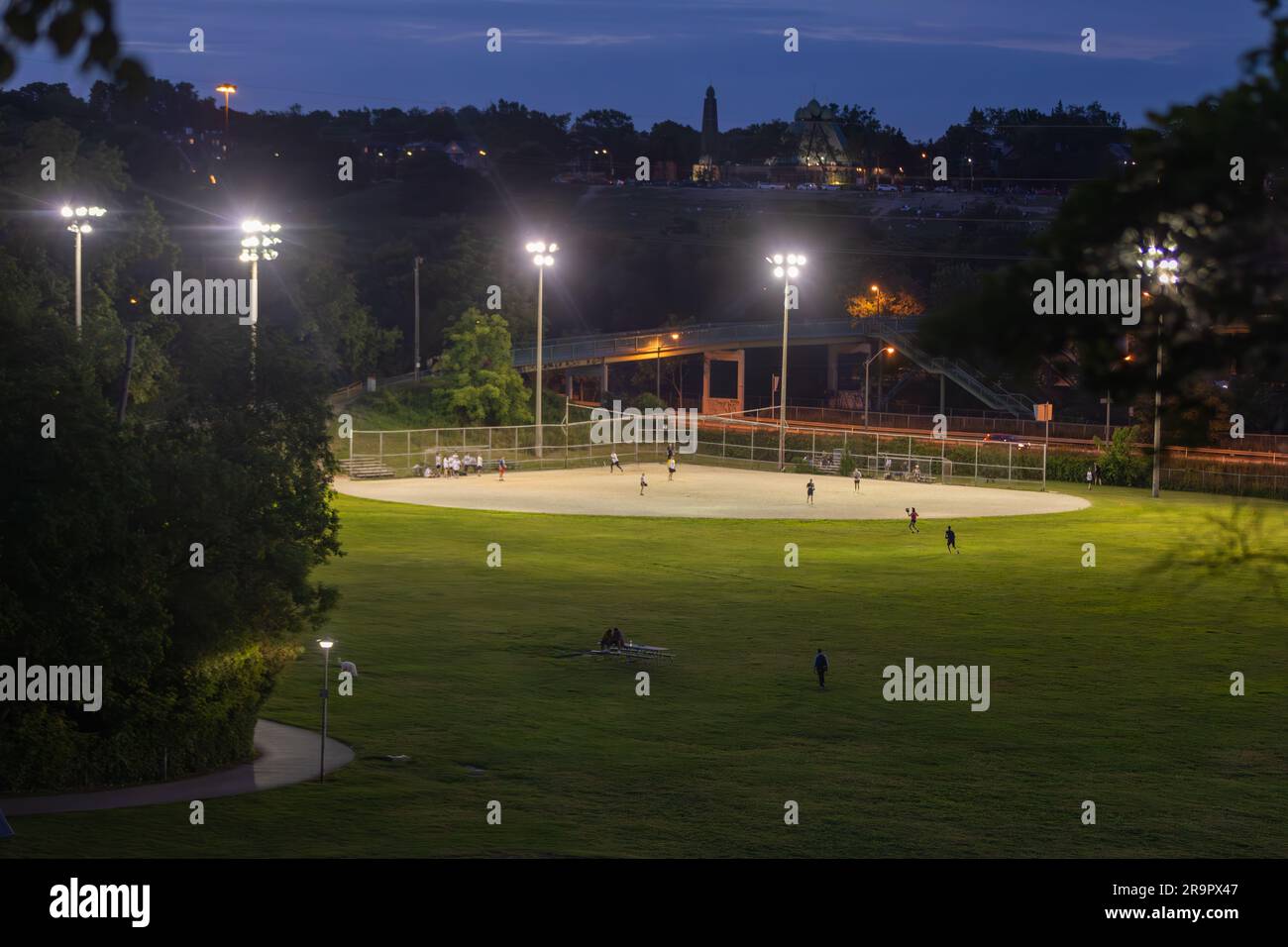 Spiel Ball! An einem schönen Sommerabend wird in einem großen Park in Toronto ein Baseballspiel der Freizeitspiele unter Lichtern gespielt Stockfoto