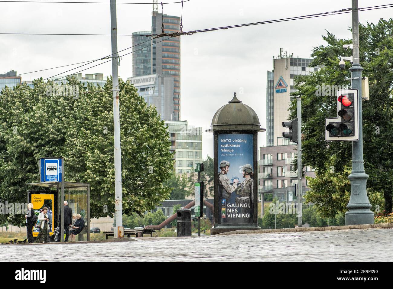 Ein Werbebanner informiert über den NATO-Gipfel 2023 im Zentrum von Vilnius, der Hauptstadt Litauens, mit Menschen, die an der Bushaltestelle warten und roten Verkehr Stockfoto