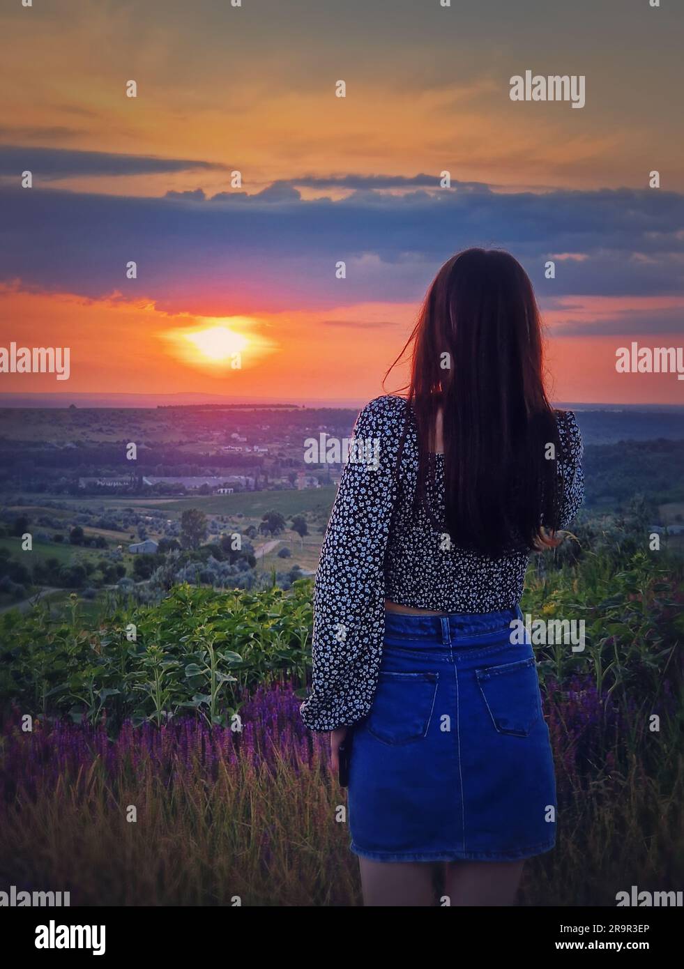 Rückansicht einer Frau im Rock, die den Sonnenuntergang über dem Tal beobachtet. Natürliche Sommerdämmerung Stockfoto