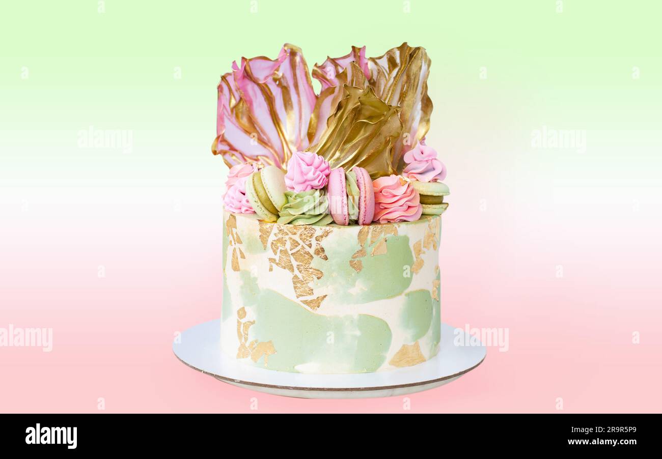 Wunderschöner rosa-grüner Käsekuchen mit Reispapier, essbarem Gold und Makronen. Köstlicher Geburtstagskuchen isoliert. Stockfoto