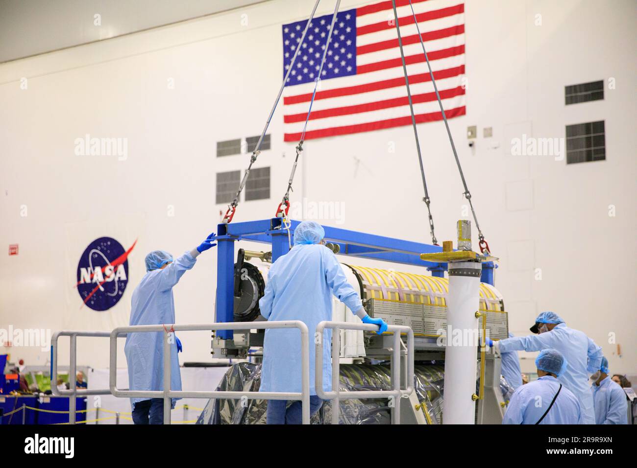 IROSA Hubbetrieb. Im Hochregal der Space Station Processing Facility im Kennedy Space Center der NASA in Florida helfen Techniker, wenn am 23. März 2023 ein Kran zum Absenken einer Reihe von International Space Station Roll Out Solar Arrays (iROSA) auf eine Plattform verwendet wird. Sie werden für die Lieferung an die Raumstation an Bord des Spediteurs Dragon von SpaceX vorbereitet, der 28. kommerzielle Rücklieferungsdienste (CRS-28) des Unternehmens zur Raumstation durchführt. IROSA ist eine neue Art von Solarpaneelen, die sich im Raum öffnen lassen und kompakter als aktuelle starre Platten sind. Stockfoto
