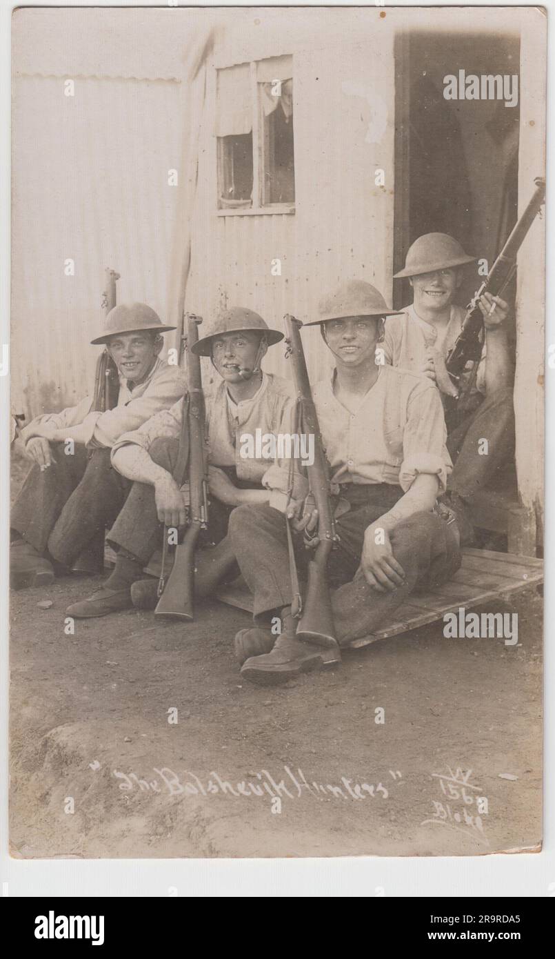 "Die Bolschewiken-Jäger": Foto von vier britischen Soldaten in Brodie-Helmen mit Gewehren, die vor einem gewellten Eisengebäude sitzen, möglicherweise einer Nissen-Hütte. Das Foto wurde wahrscheinlich kurz nach dem Ende des Ersten Weltkriegs aufgenommen, als britische Soldaten nach Russland geschickt wurden, um in den russischen Bürgerkrieg einzugreifen Stockfoto
