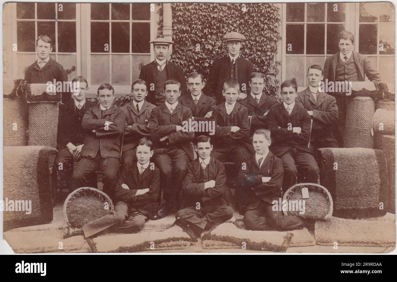 Foto einer Gruppe von Männern und Jungen aus dem frühen 20. Jahrhundert, die in einer Teppichfabrik beschäftigt waren. Sie werden außerhalb des Fabrikgebäudes aufgestellt und zeigen Beispiele ihrer Arbeiten auf dem Boden Stockfoto