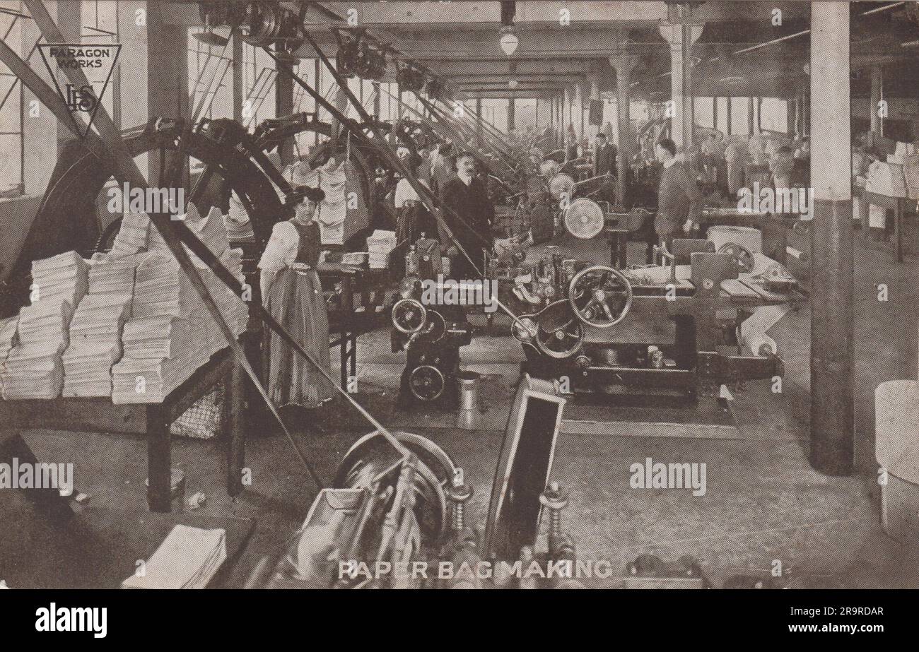 Papiertütenherstellung: Anfang des 20. Jahrhunderts Postkarte hergestellt vom Hersteller Lamson Paragon Supply Co., Ltd., 5 Cabinet Chambers, Basinghall Street, Leeds. Das Foto zeigt die Fabrikhalle, wo Männer und Frauen an den Maschinen stehen. Zwischen den Maschinen befinden sich große Papierstapel auf Tischen. Stockfoto