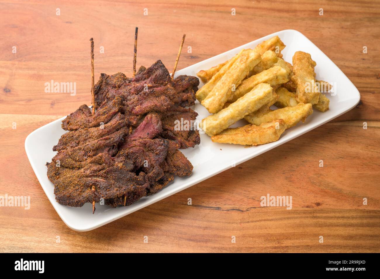 Ein saftiger Teller mit Pommes Frites und Rindfleisch auf einem rustikalen Holztisch, die perfekte Kombination für eine herzhafte Mahlzeit Stockfoto