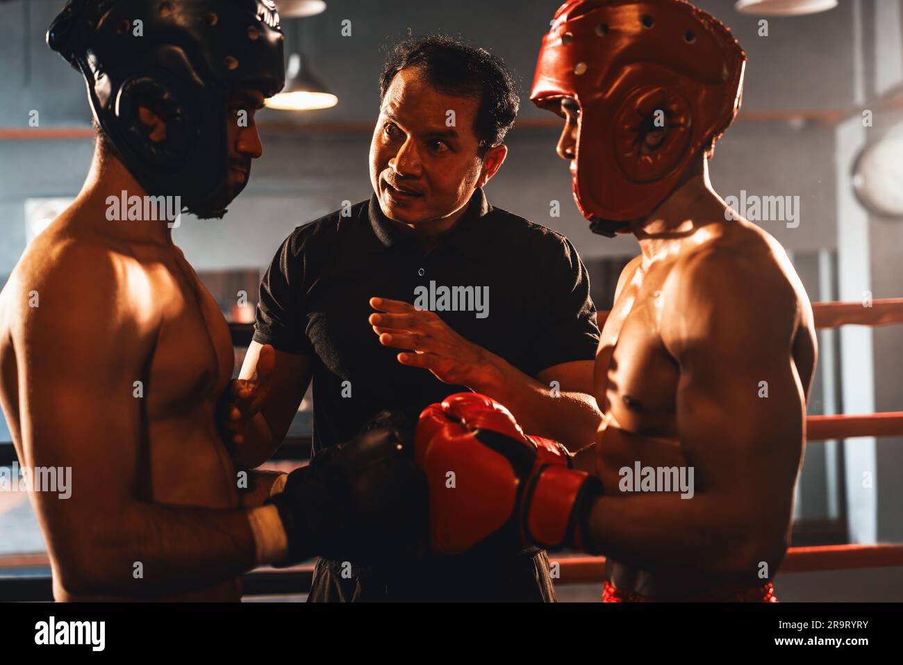 Ein Boxer mit Schutzhelm oder Kopfschutz zeigt sich aneinander, während der Schiedsrichter dem Gegner die Regeln für die Interaktion erklärt, bevor er mit dem Boxkampf beginnt Stockfoto