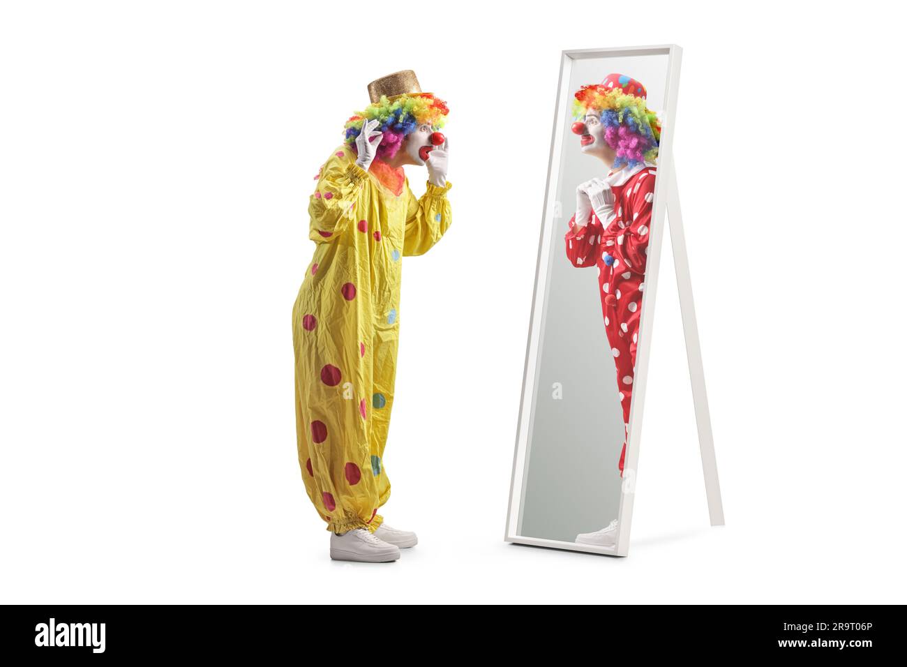 Ein Clown in einem gelben Kostüm steht vor einem Spiegel und sieht einen Clown in einem roten Kostüm isoliert auf weißem Hintergrund Stockfoto