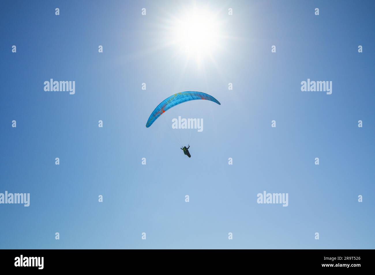 Silhouette eines Fallschirmspringers mit offenem Fallschirm, der in der Luft fliegt, und heller Sonne und blauem Himmel im Hintergrund, Kopierraum Stockfoto