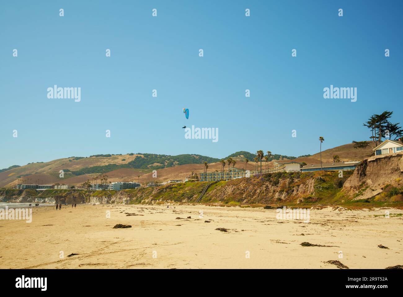 Pismo Beach Klippen und Silhouette eines Fallschirmspringers mit offenem Fallschirm und hellblauem Himmel im Hintergrund, kalifornische Küste Stockfoto