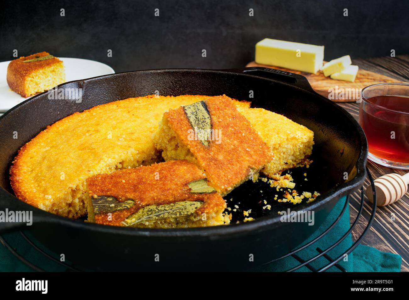 Salbei-Maisbrot in Stücke geschnitten in einer gusseisernen Pfanne: Frisch gebackenes südliches Buttermilch-Maisbrot in einer Pfanne mit Butter und Honig Stockfoto